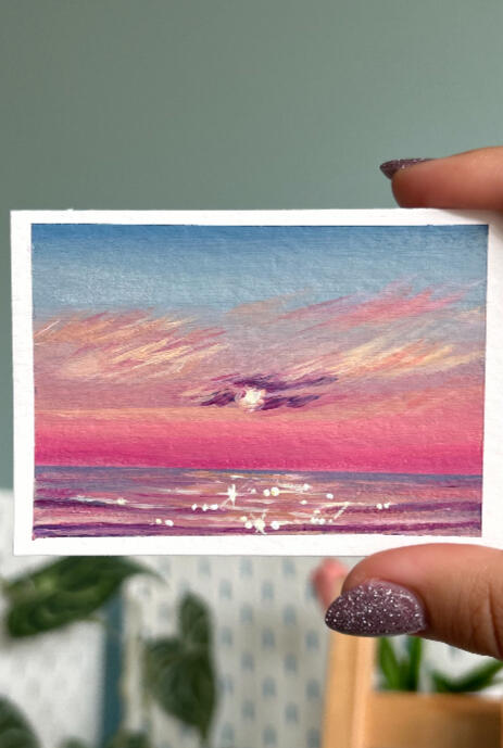 pink glow mini hand holding aceo size painting on paper of a pink sunset over a pink glowing seascape horizon