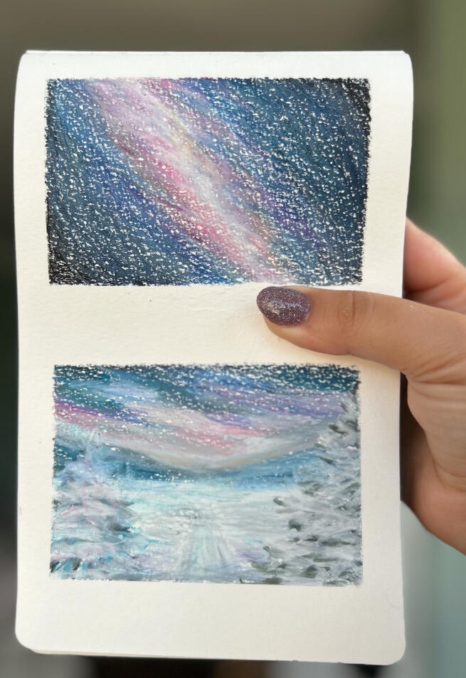 starry nights hand holding sketchbook page featuring two mini paintings made with wax pastels. The painting on top, features a dark sky with visible galaxy imagined by the artist, the painting at the bottom represents a snowy landscape with trees and starry night sky